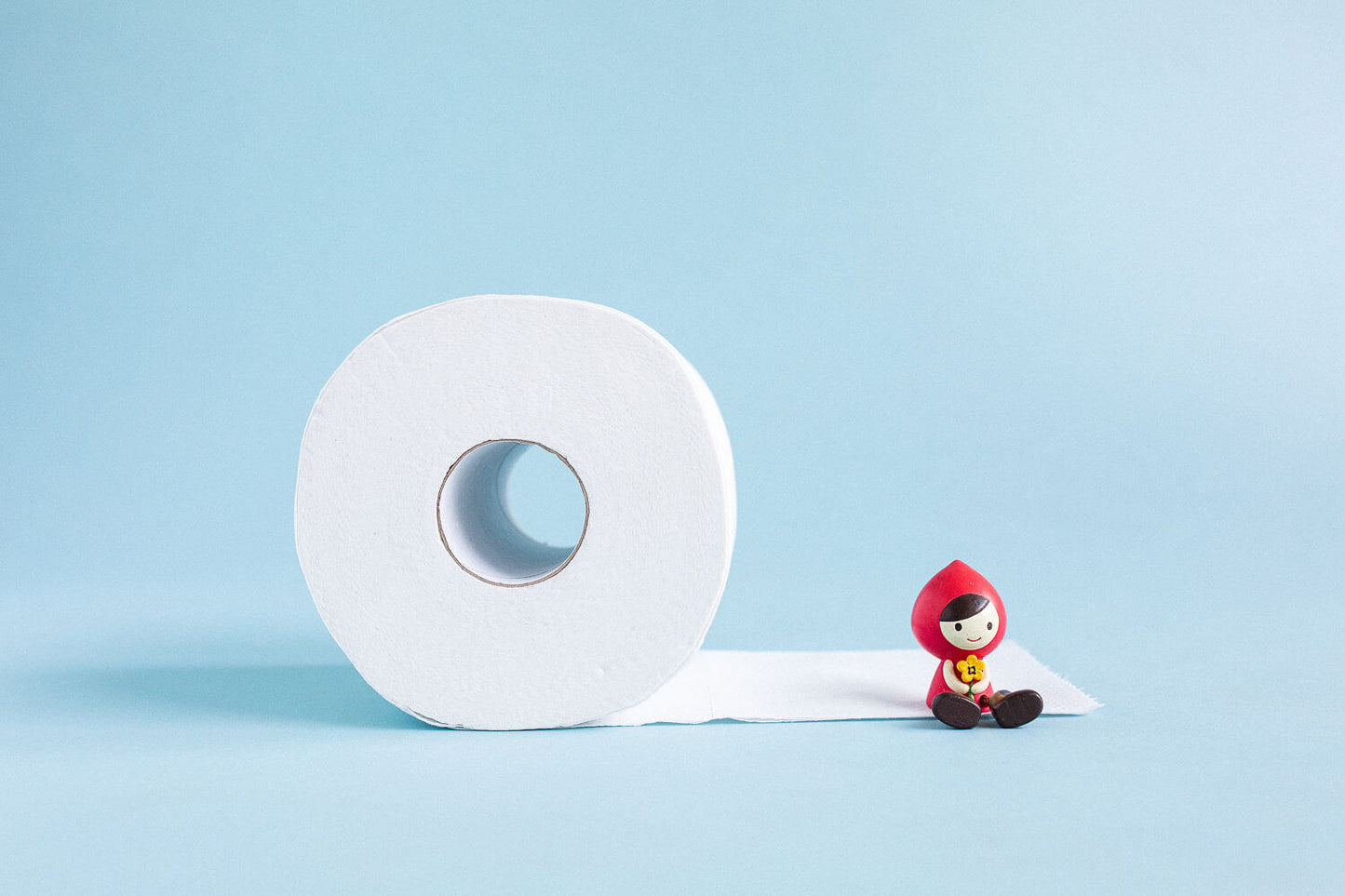eco toilet paper with a portion unrolled on the ground. A small red toy girl figurine sitting on the unrolled portion.