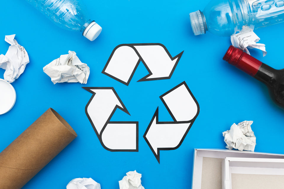 recyclable materials such as paper, plastic and glass surrounding a while recycle symbol printed on a blue background